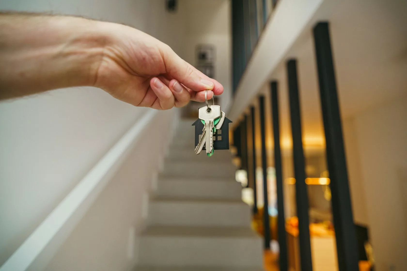 Mano sosteniendo unas llaves con llavero en forma de casa frente a una escalera