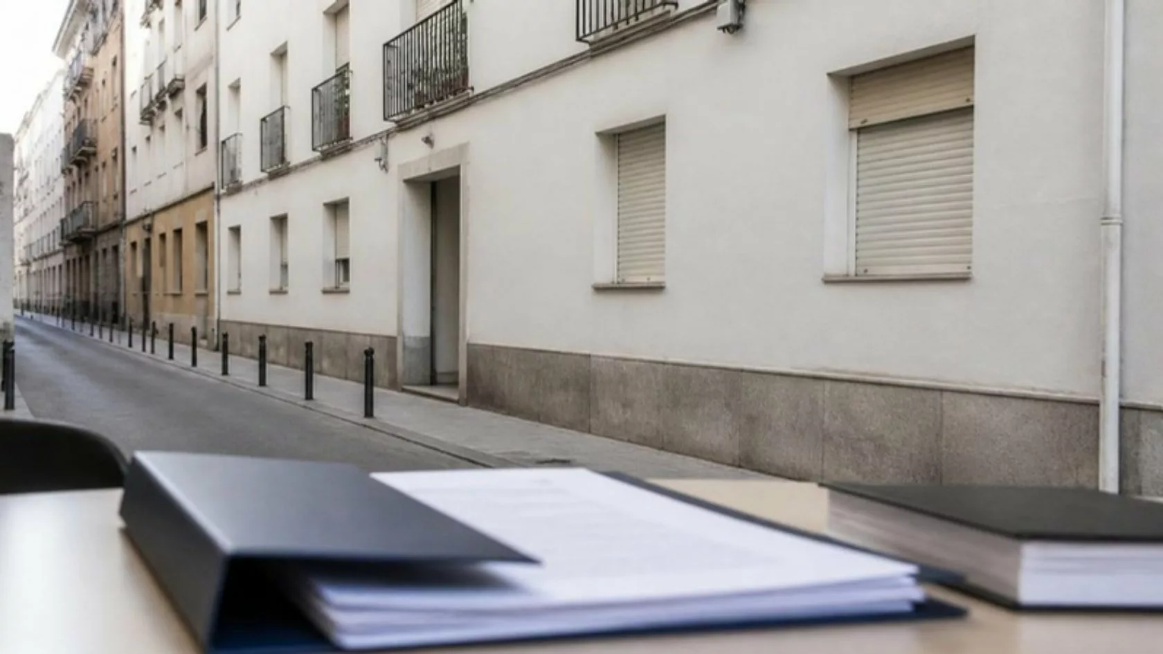 Edificio residencial en una calle de una ciudad española con documentos legales en primer plano, inversión en inmuebles ocupados